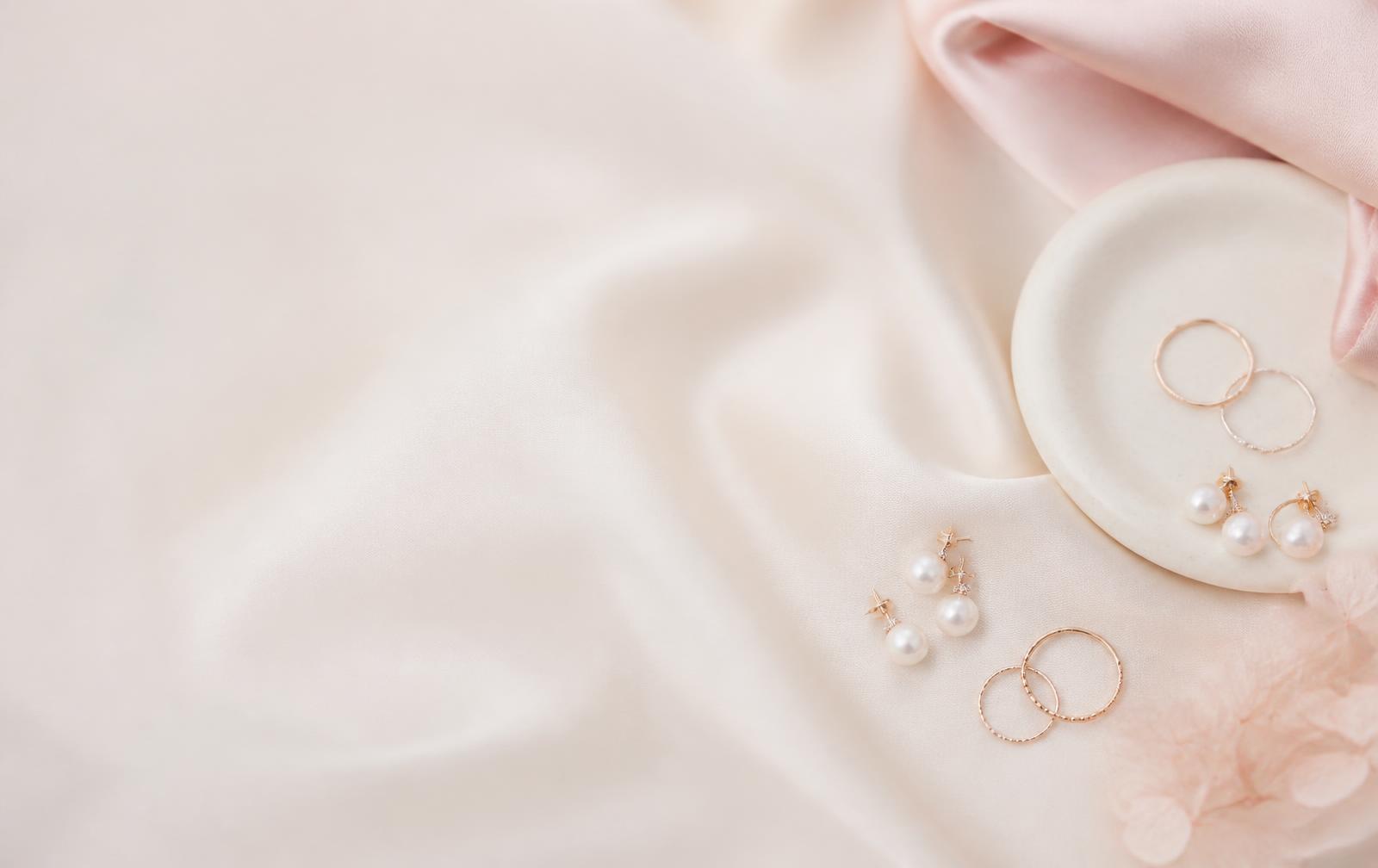 Pearl earrings and thin gold rings on cream silk